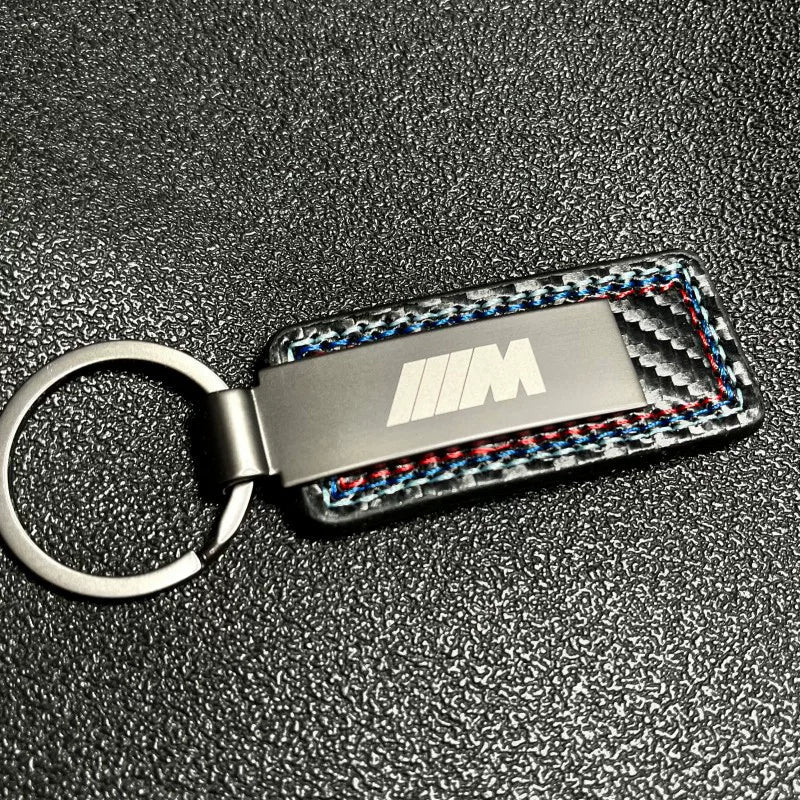 BMW M carbon fiber keychain on dark textured background