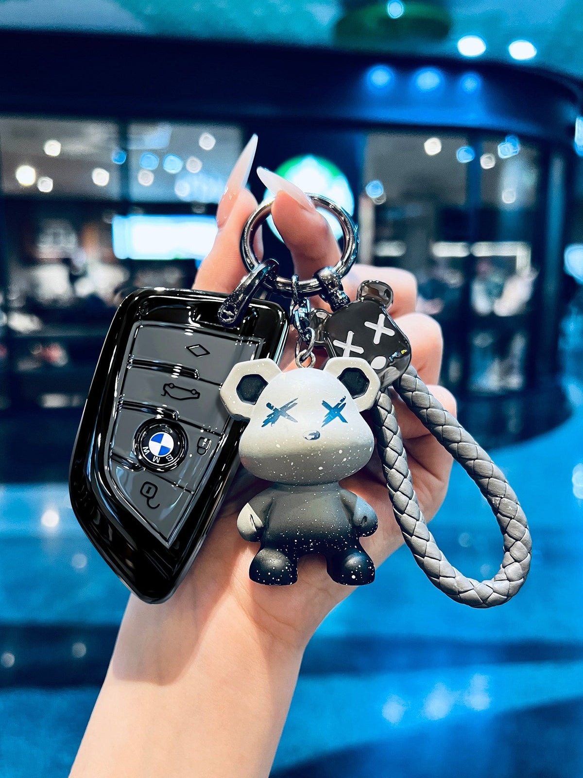 BMW glossy black TPU key fob case with gray bear-shaped keychain charm held in hand
