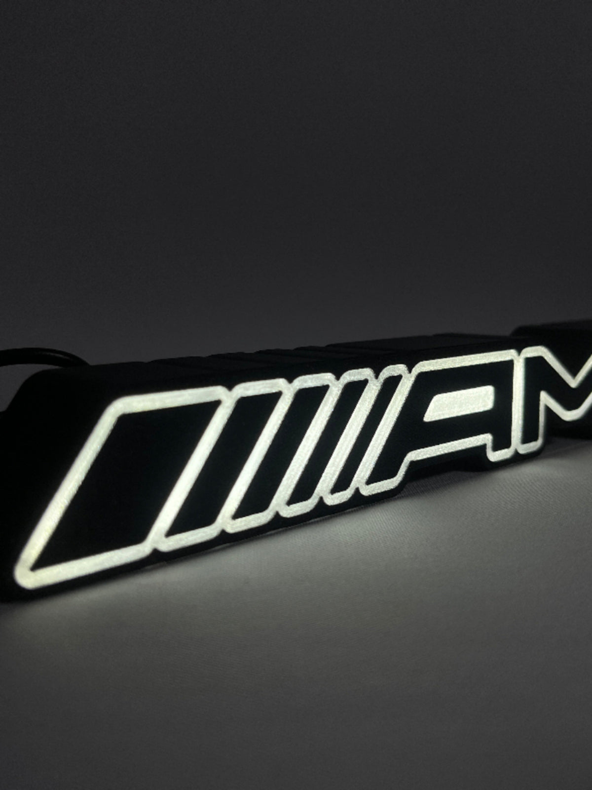 Mercedes-AMG LED emblem lamp lit up – angled close-up of the glowing AMG stripes