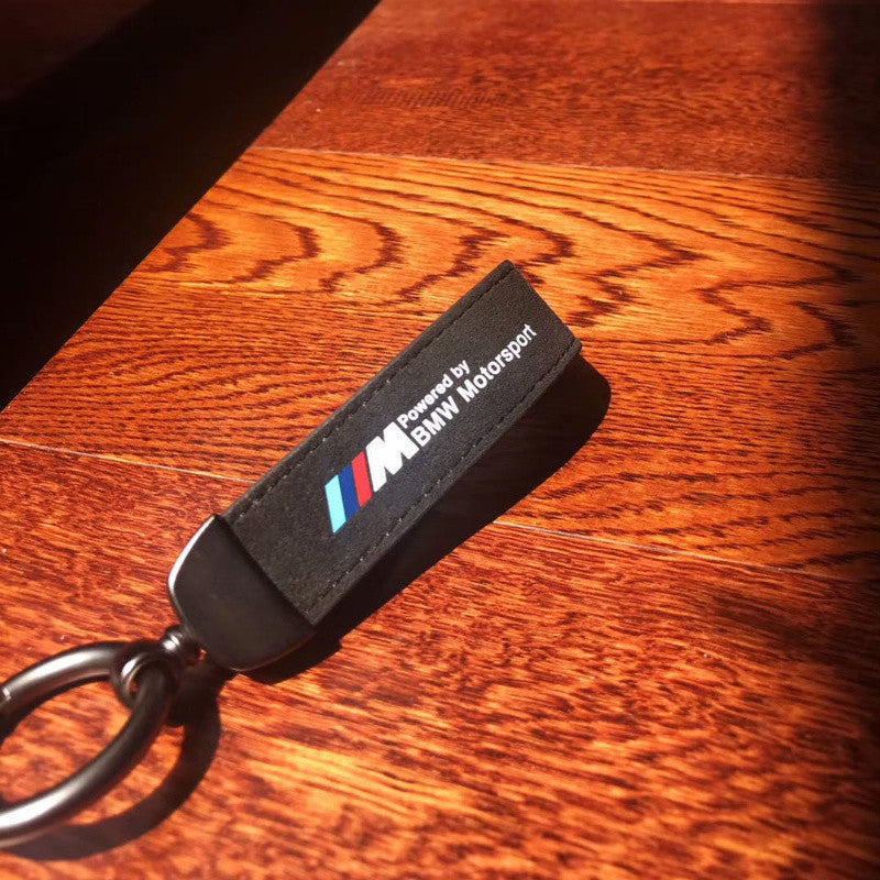 Black BMW Motorsport suede keychain with metal ring on wooden table