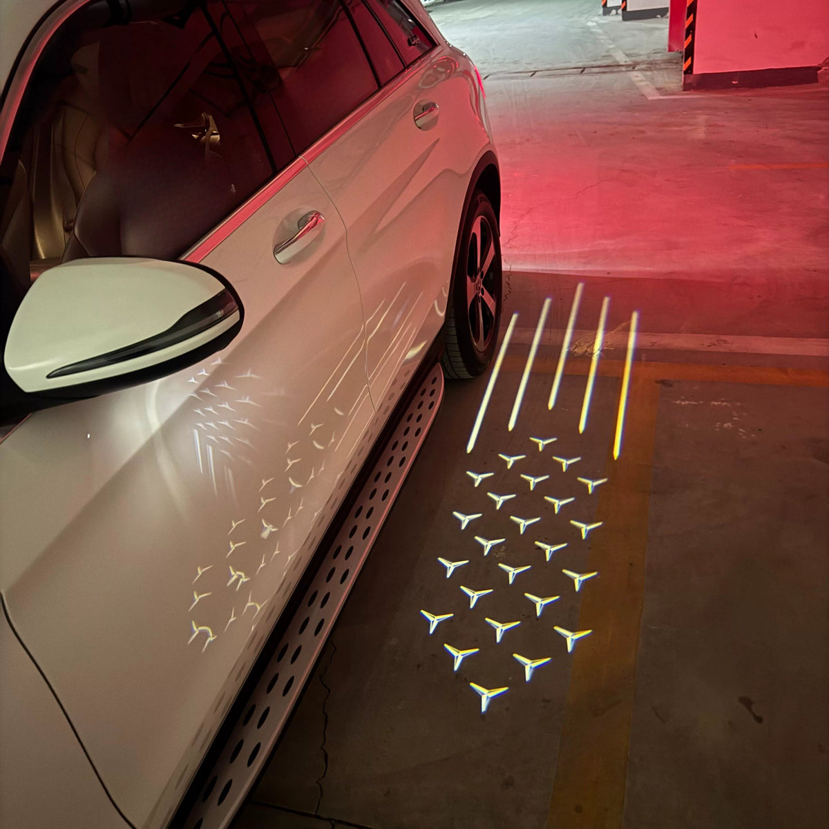 Mercedes-Benz Starfall mirror welcome light projecting shooting-star trails and three-pointed stars beside a white Mercedes SUV